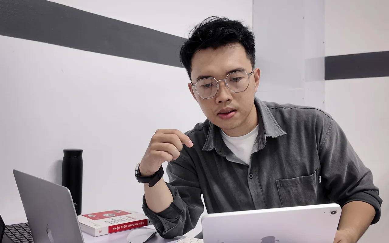 Quốc Hiệp làm việc với laptop và máy tính bảng tại bàn làm việc