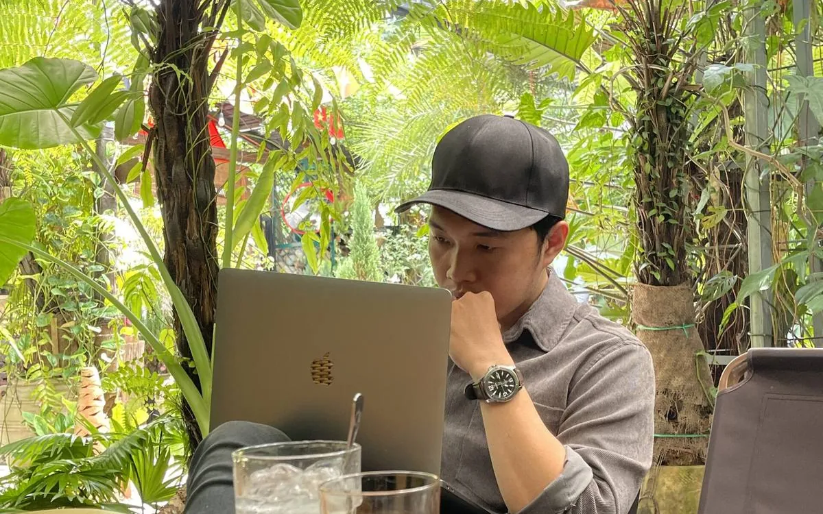 Quốc Hiệp ngồi làm việc với laptop trong một quán cà phê sân vườn